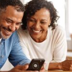 Casal negro sorrindo ao olhar um celular. LCbank: escolha estratégica para quem antecipa RPV.